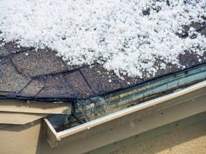 Hail on a roof with water running into a gutter.
